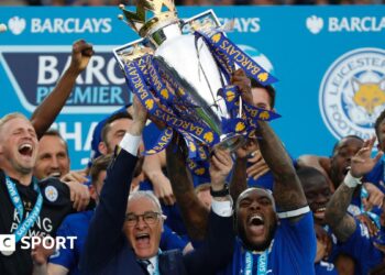 Leicester City manager Claudio Ranieri and captain Wes Morgan lift the Premier League trophy while surrounded by euphoric Foxes players
