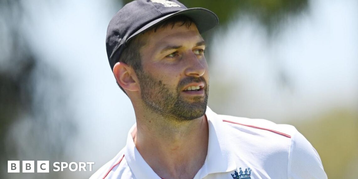 Mark Wood, wearing a blue England cap, looks to the side