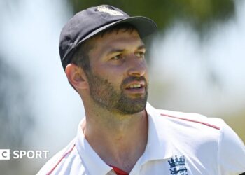 Mark Wood, wearing a blue England cap, looks to the side