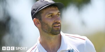 Mark Wood, wearing a blue England cap, looks to the side