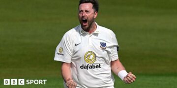 Ollie Robinson, wearing a white Sussex shirt, roars and clenches both of his fists in front of him to celebrate a wicket
