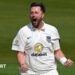 Ollie Robinson, wearing a white Sussex shirt, roars and clenches both of his fists in front of him to celebrate a wicket