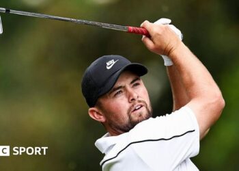 Alex Fitzpatrick watches his ball after playing an iron shot, with the club above his head