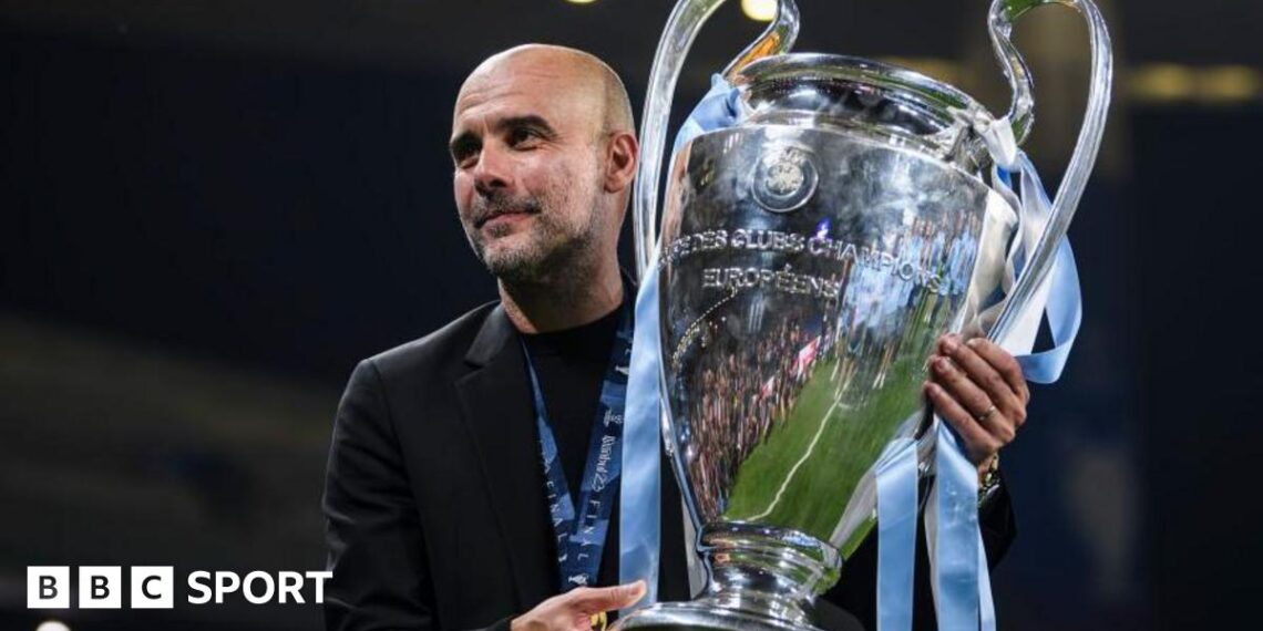 Pep Guardiola holds the Champions League trophy, which is adorned with Manchester City light blue ribbons