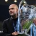 Pep Guardiola holds the Champions League trophy, which is adorned with Manchester City light blue ribbons