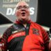 Stephen Bunting celebrates, pointing with both index fingers and pulling a celebratory facial pose as he wears a black and red darts shirt