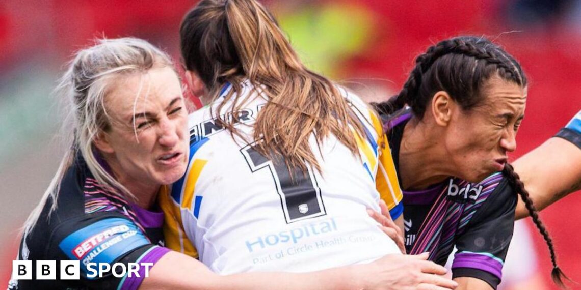 Leeds player Ruby Enright, with a white shirt bearing the number one, is tackled by St Helens players Jodie Cunningham (left) and Zoe Harris (right), both wearing black with purple trim,