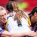 Leeds player Ruby Enright, with a white shirt bearing the number one, is tackled by St Helens players Jodie Cunningham (left) and Zoe Harris (right), both wearing black with purple trim,