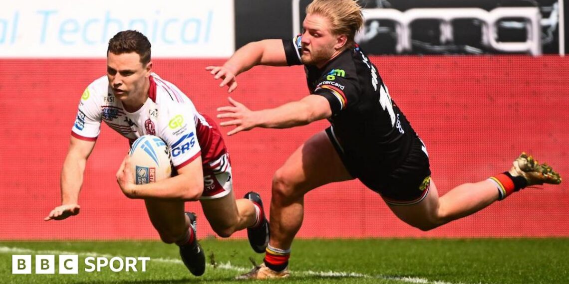 Wigan Warriors full-back Jai Field, in white and red, dives over the line to score a try as a Bradford player tries to tackle him