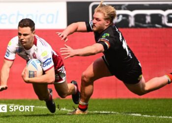 Wigan Warriors full-back Jai Field, in white and red, dives over the line to score a try as a Bradford player tries to tackle him
