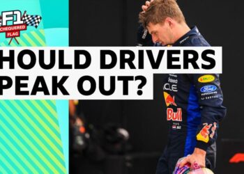 Max Verstappen dressed in Red Bull race suit with a hand to his head