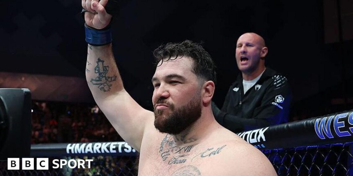 Louie Sutherland holds up his arm as he stands in the octagon