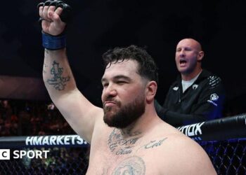 Louie Sutherland holds up his arm as he stands in the octagon