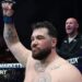 Louie Sutherland holds up his arm as he stands in the octagon