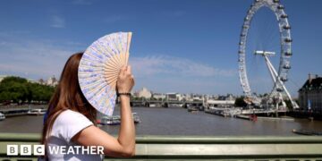 Woman fans herself on a hot sunny day in London with the London Eye in the background