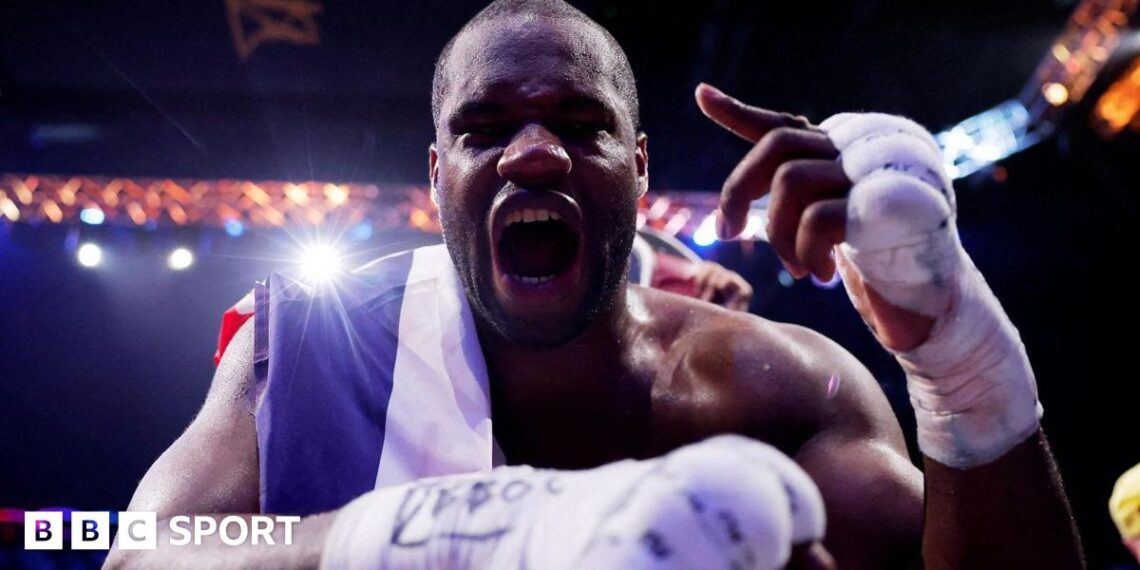 Daniel Dubois leans over the ropes of a boxing ring and holds up his hand