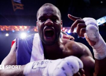 Daniel Dubois leans over the ropes of a boxing ring and holds up his hand