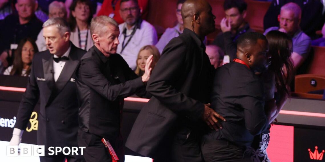A female spectator (right) is escorted out of the arena at the Crucible Theatre in Sheffield after jumping the barrier between the seats and the playing area