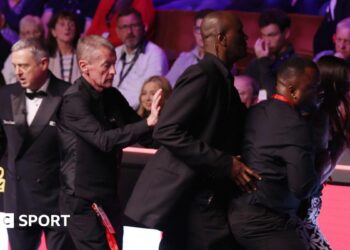 A female spectator (right) is escorted out of the arena at the Crucible Theatre in Sheffield after jumping the barrier between the seats and the playing area