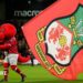 Mascot Wrex the Dragon carries a Wrexham flag across the pitch