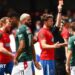Paul Rutherford is shown a red card with his back to the camera showing his name and number in Wrexham's green away shirt, with Dagenham players in red shirts around the referee.