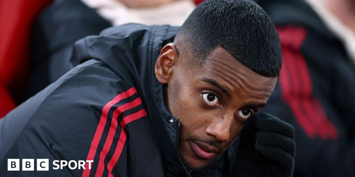 Alexander Isak looks on from the bench in a zip-up dark jacket with red stripes before the Champions League game between Liverpool and PSV Eindhoven at Anfield on 26 November, 2025