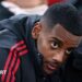 Alexander Isak looks on from the bench in a zip-up dark jacket with red stripes before the Champions League game between Liverpool and PSV Eindhoven at Anfield on 26 November, 2025