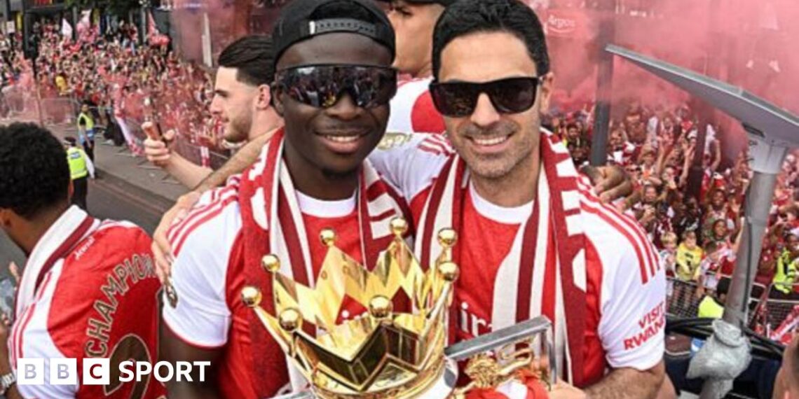 Bukayo Saka and Mikel Arteta, both in sunglasses and red and white team kit, with the Premier League trophy on Arsenal's bus parade