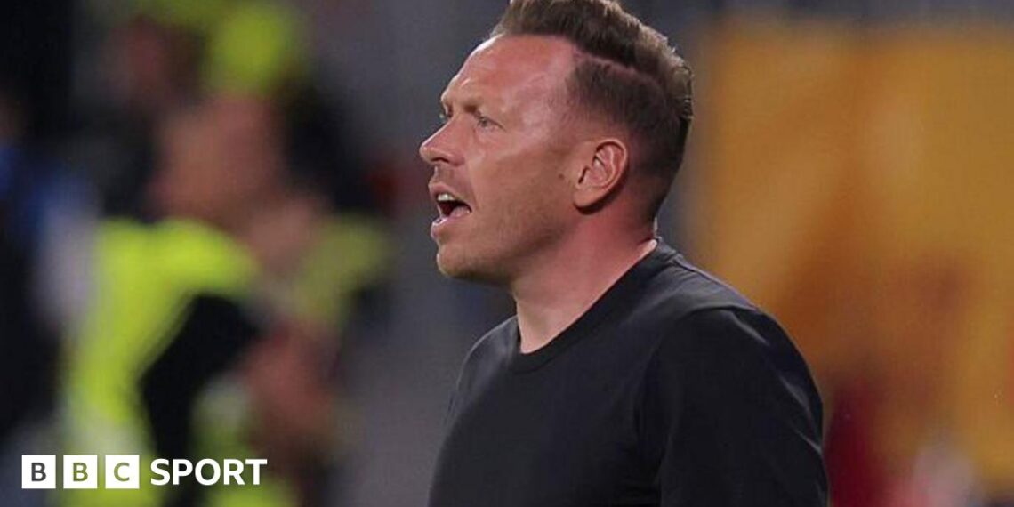 Wales boss Craig Bellamy reacts with an open-mouthed expression as he stands in a round-neck black top