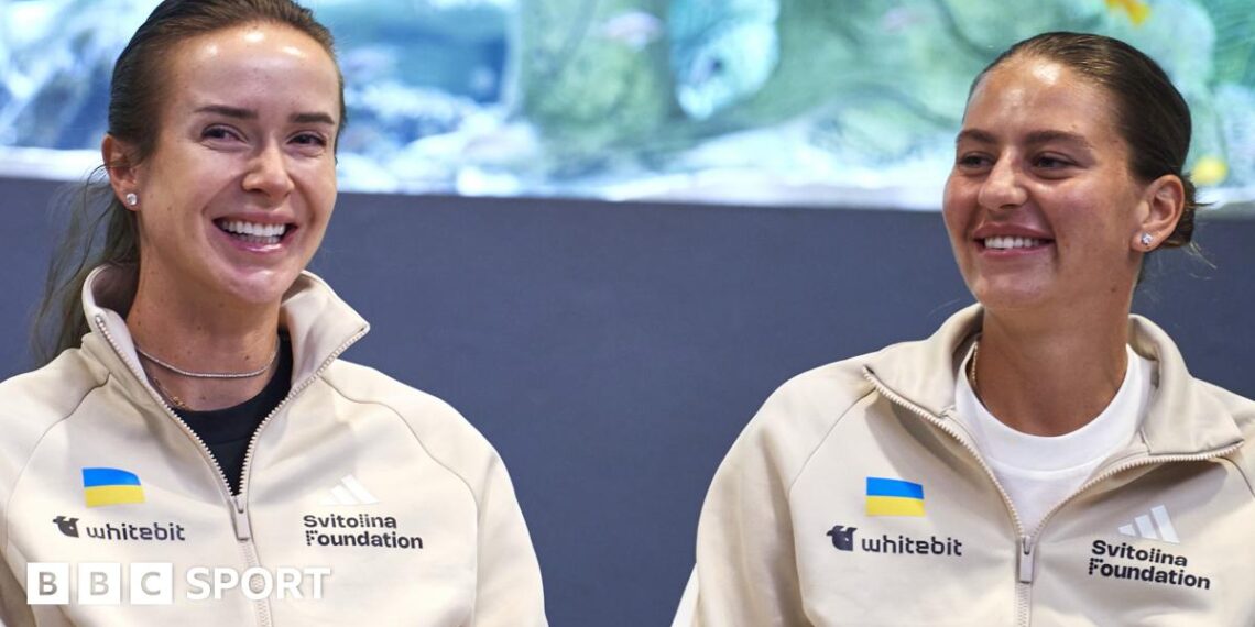 Elina Svitolina and Marta Kostyuk sit together and smile wearing cream zip-up jackets
